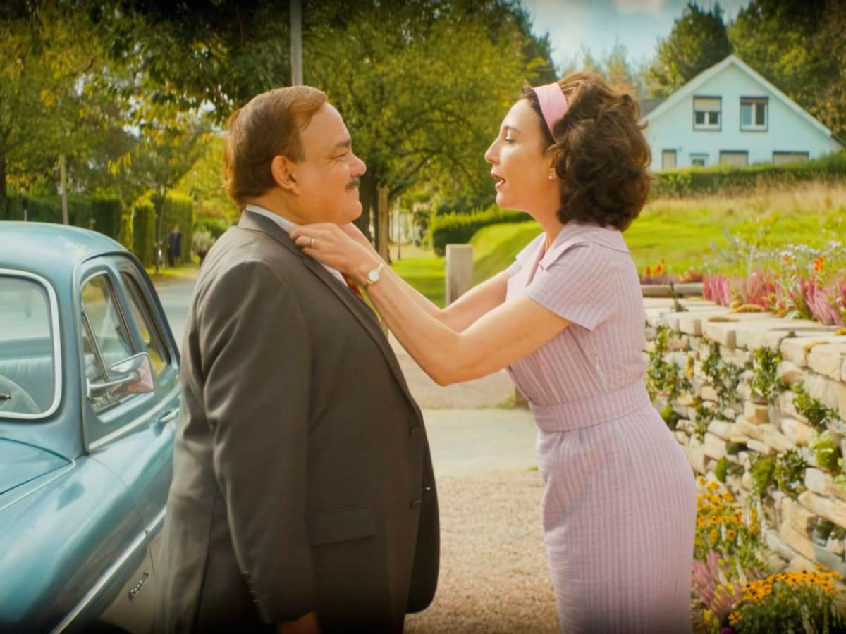 Une femme ajuste le col de son marie avant qu'il entre dans sa voiture.