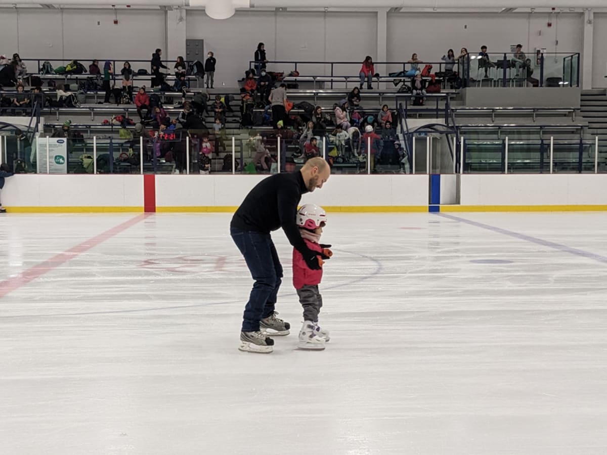 Une personne accompagne un enfant qui apprend à patiner.