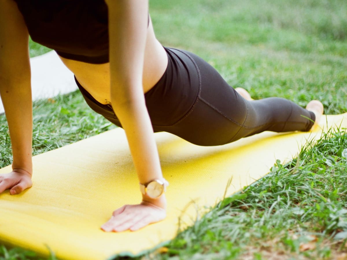 Une personne fait une posture de yoga sur un tapis dans un parc.