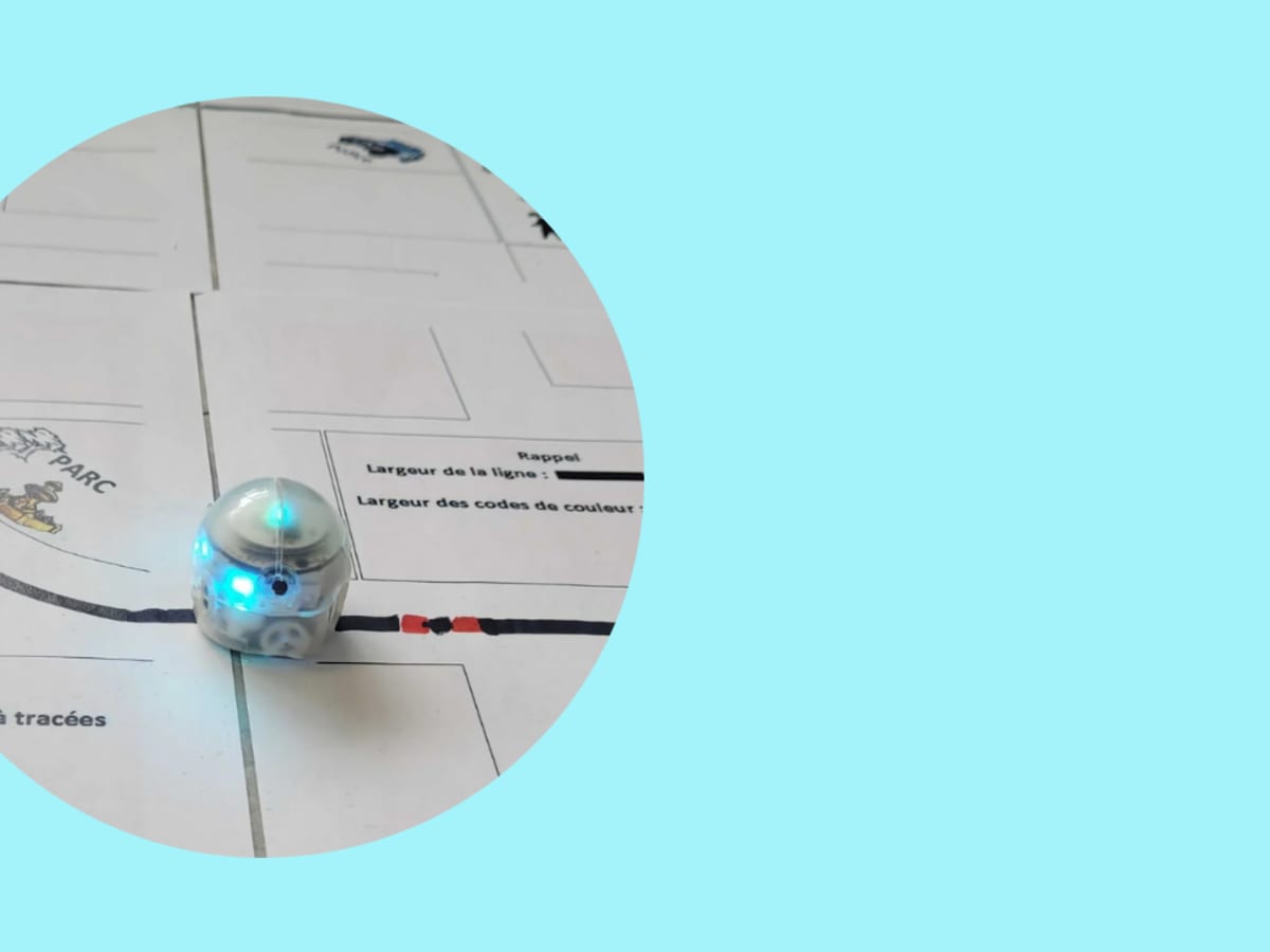 Petit robot programmable muni de lumières bleues circulant sur un parcours tracé sur papier. L’image évoque une activité ludique de découverte de la robotique, de la programmation et des technologies.