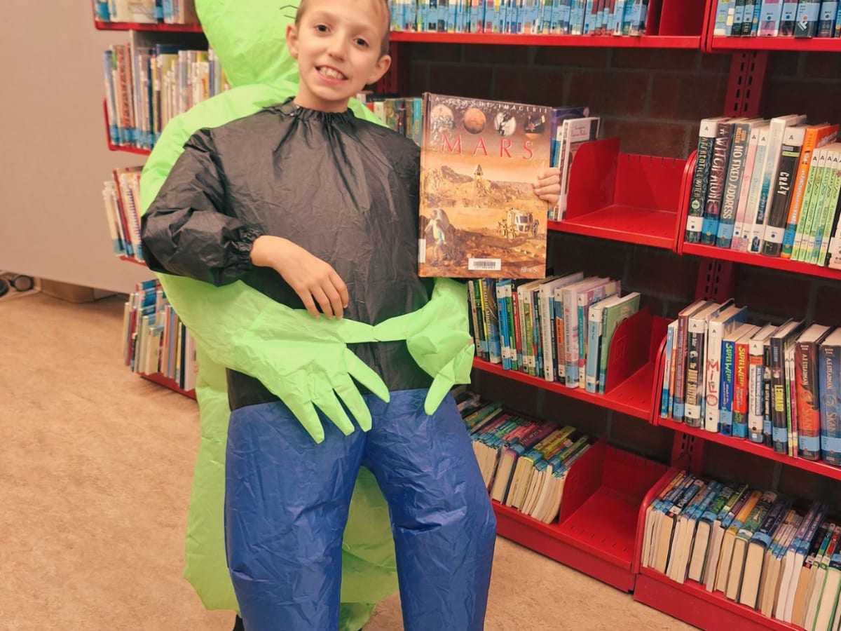 Un enfant déguisé en enlèvement d'alien tient un livre sur la planète Mars.