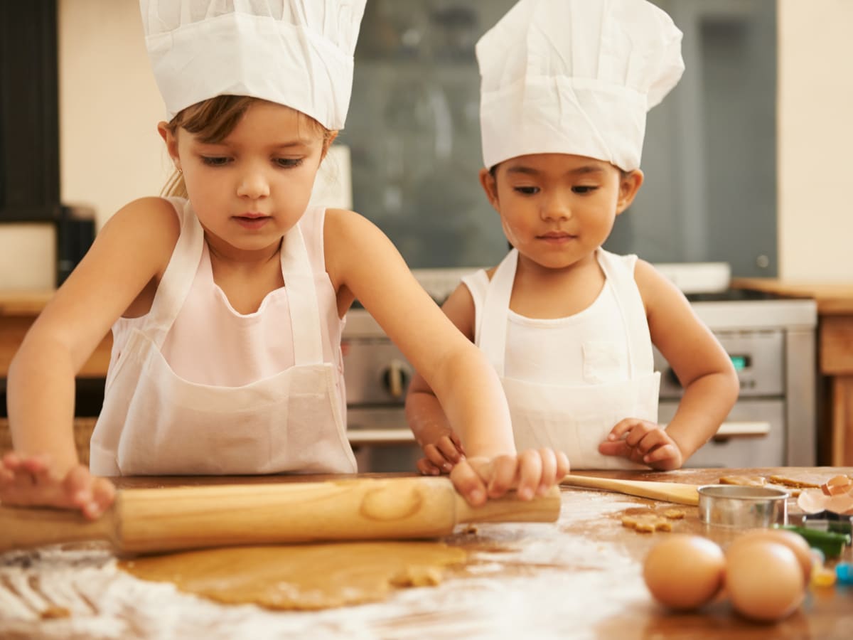 Photographie de deux enfants avec toque de chef cuisiner en train d'étaler de la pâte