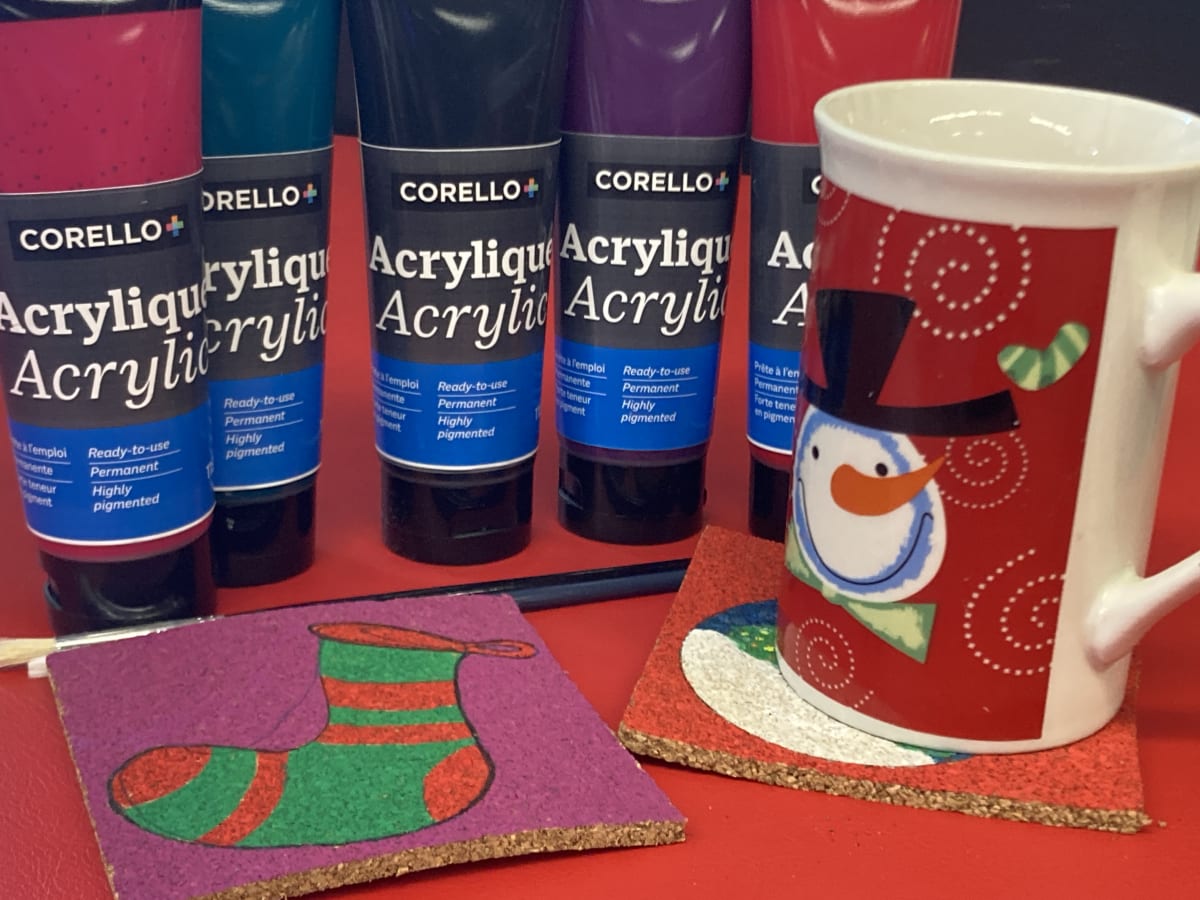 Tasse rouge des fêtes devant des pots de peintures acryliques et sous-verre en liège