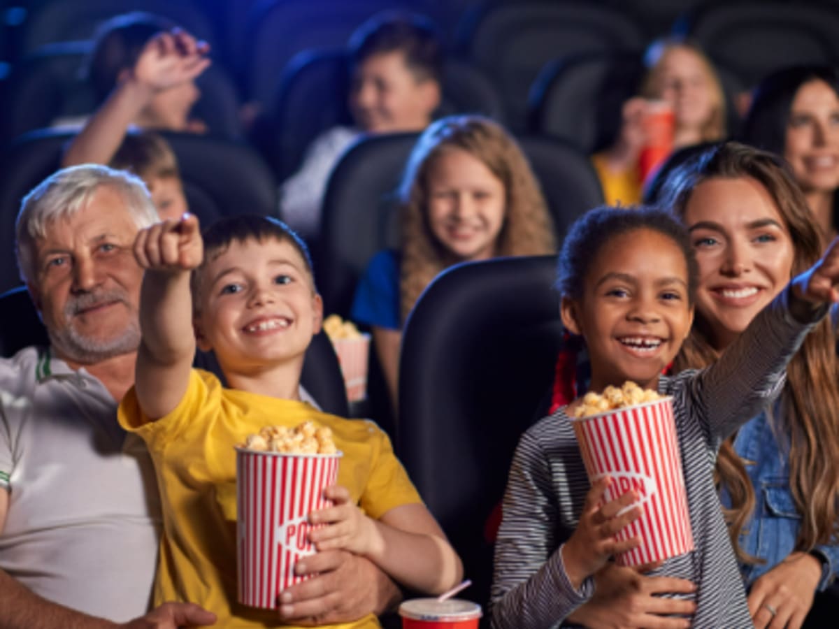 Photo d'enfants tenant des contenants de popcorn en pointant à un écran, assis sur les jambes d'adultes
