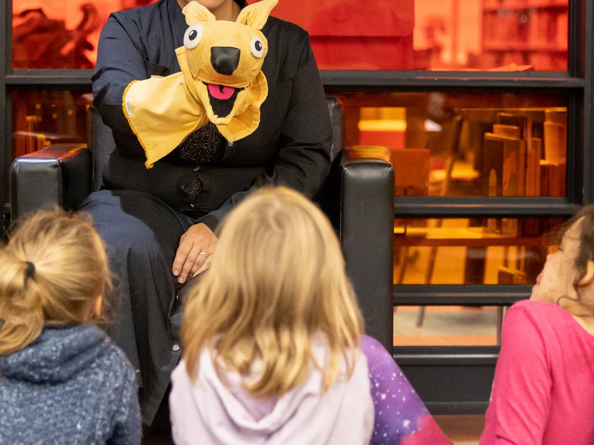 Femme avec marionnette jaune devant des enfants accroupis