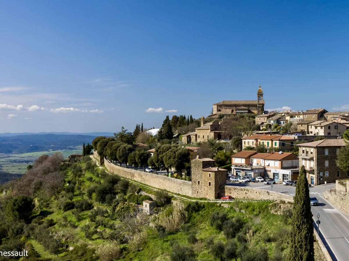 Cette photographie présente un magnifique village perché de Toscane, installé au sommet d'une colline et dominant un vaste paysage de vallées verdoyantes.