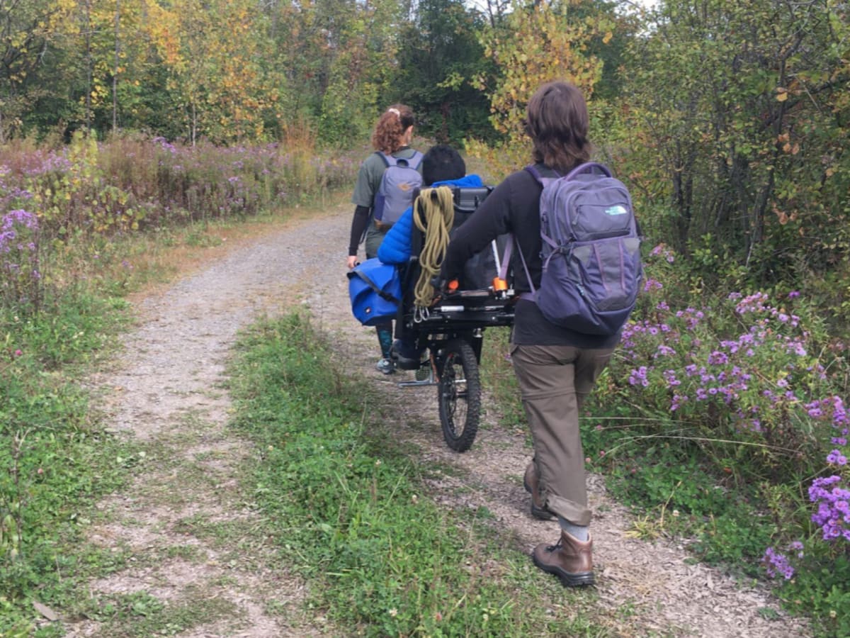 Deux personnes transportent une personne à mobilité réduite dans un sentier