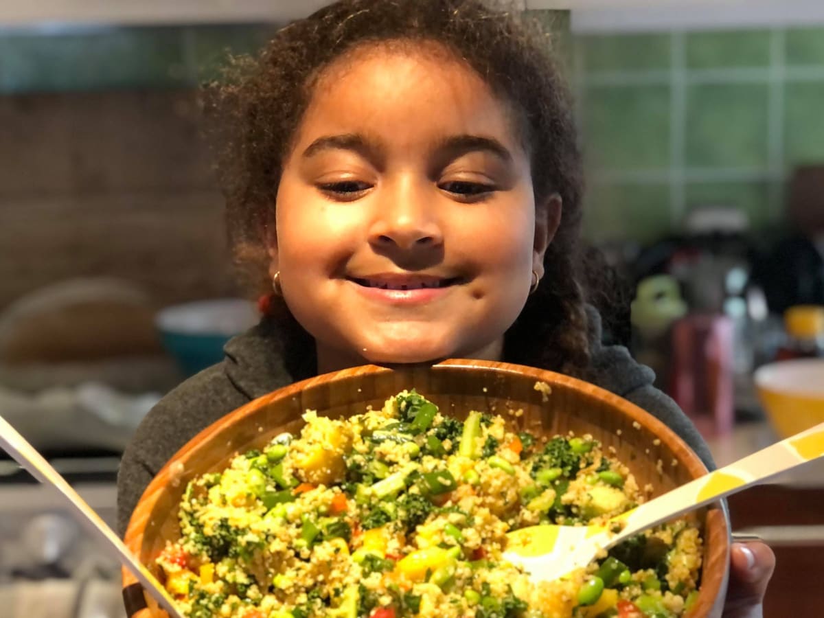 Photo d'une enfant qui tient un grand bol de couscous au légumes