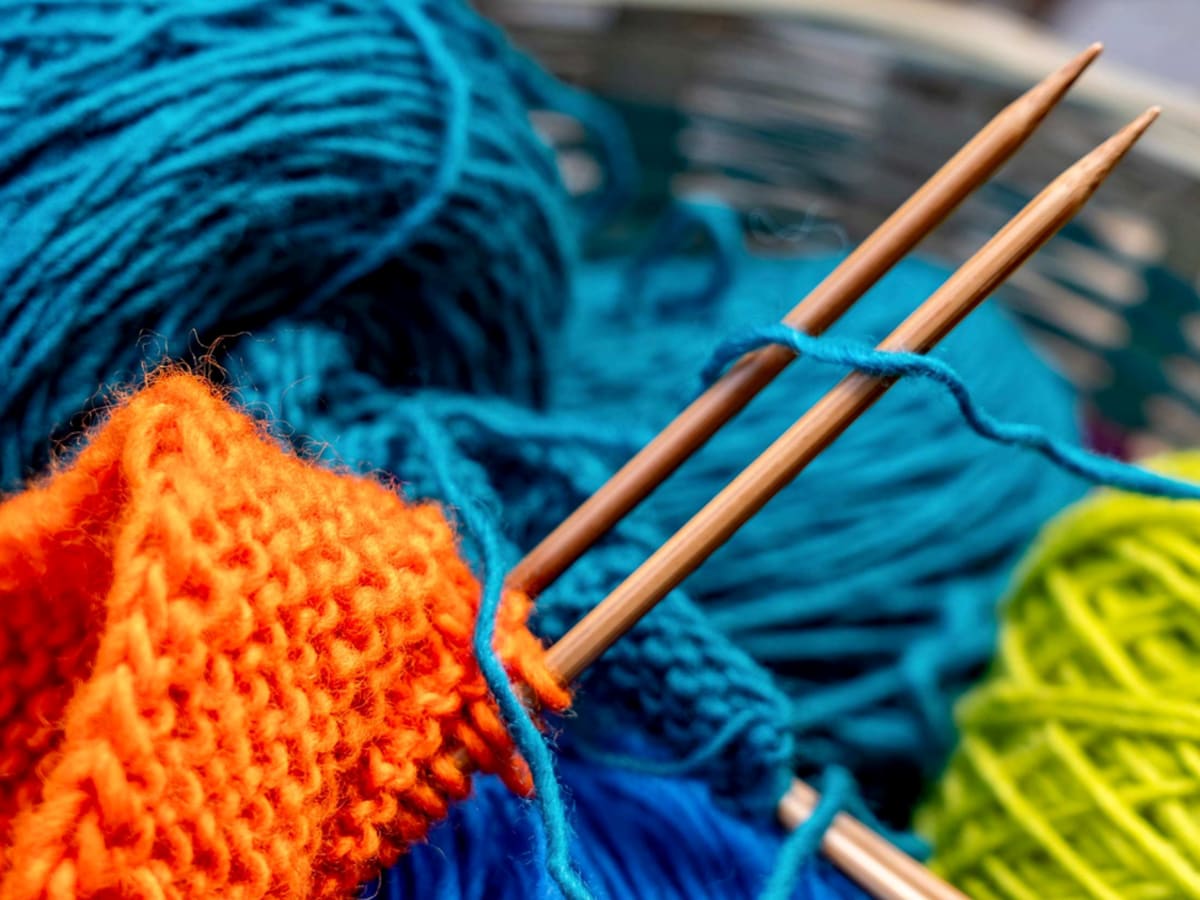 Gros plan de pelotes de laine colorées et d’un ouvrage en tricot en cours, avec 2 aiguilles à tricoter croisées.