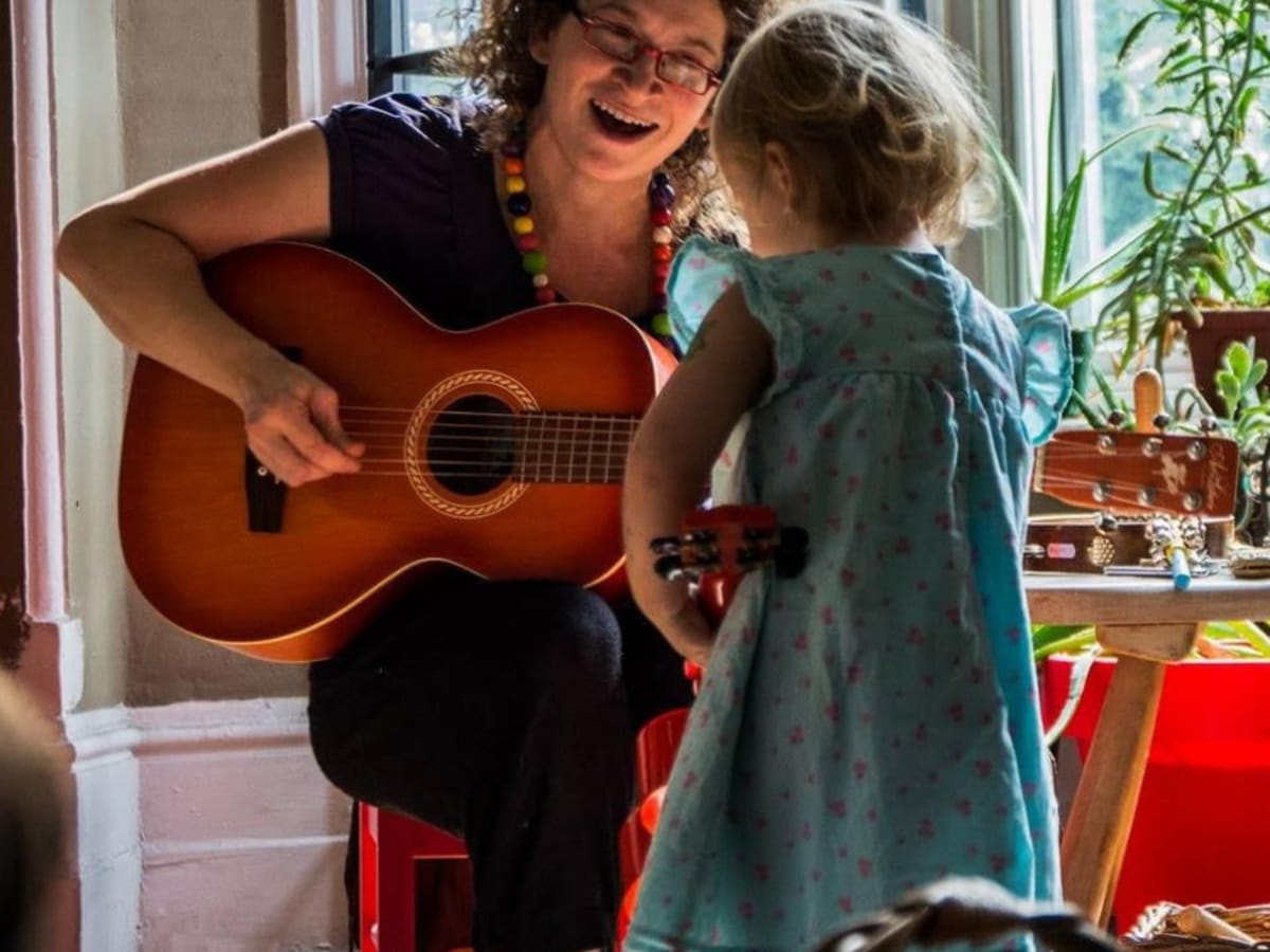 Une femme joue de la guitare en souriant pour un enfant qui est devant elle.