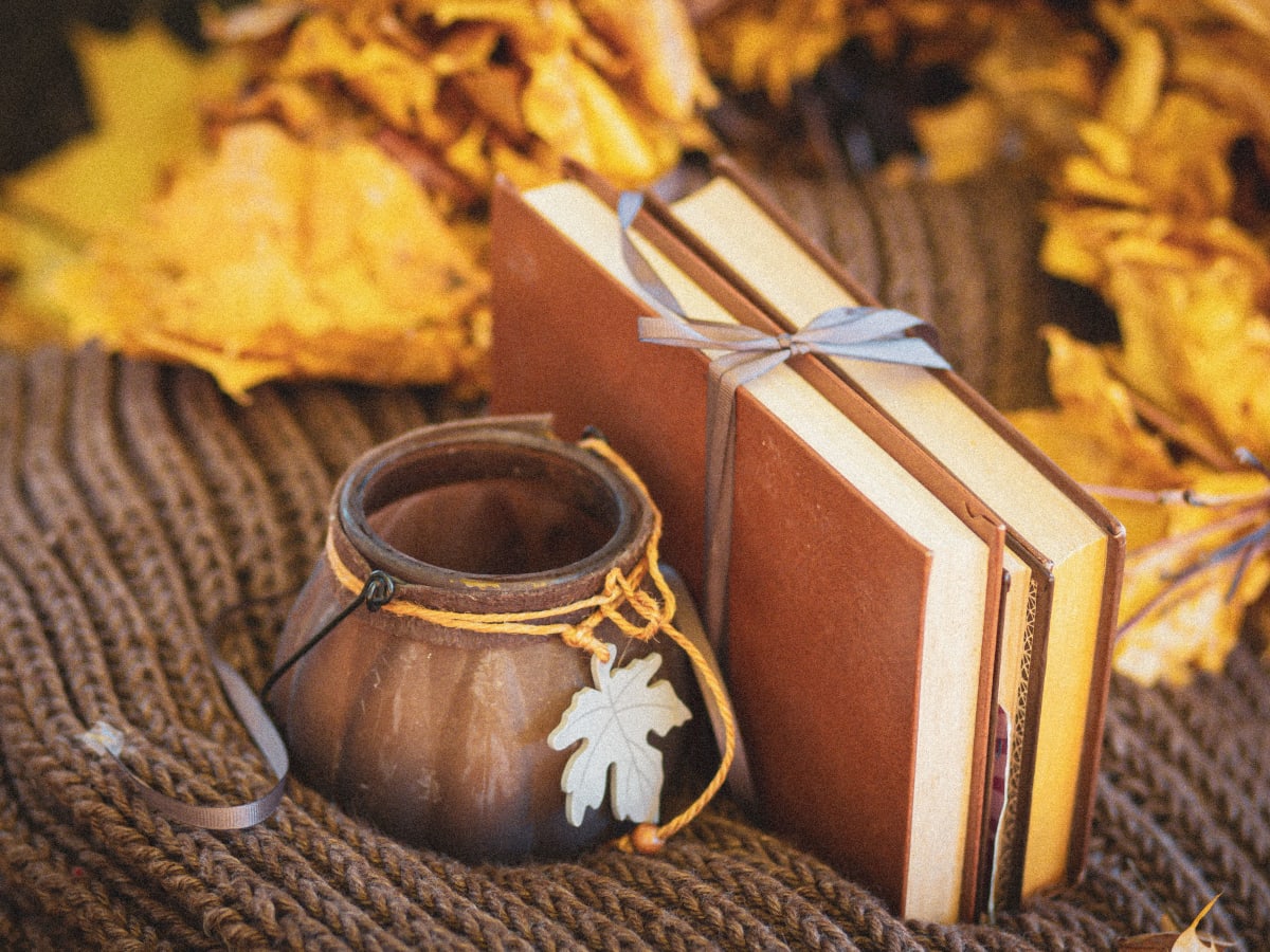 Cette image présente une nature morte aux couleurs automnales, mettant en scène des livres et des objets décoratifs dans une ambiance chaleureuse et propice à la lecture.