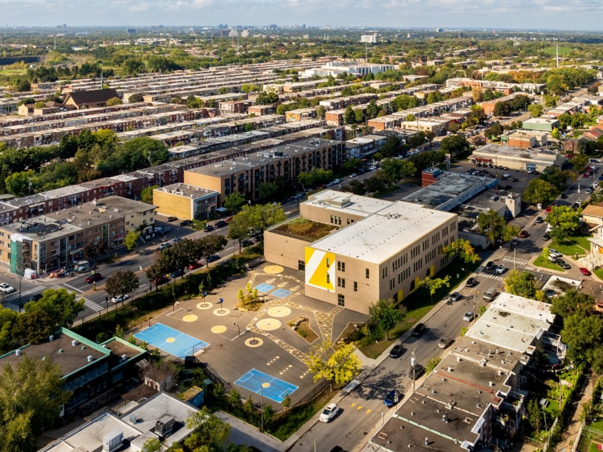 Vue aérienne d'un quartier avec en son centre une école récemment rénovée avec une cour présentant de la peinture au sol dans des tons de bleu et de jaune
