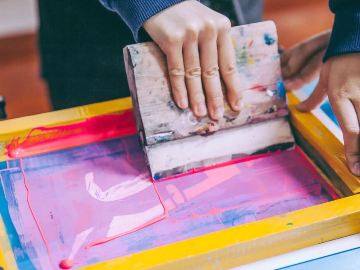 Personne appliquant de la peinture sur un cadre de sérigraphie.