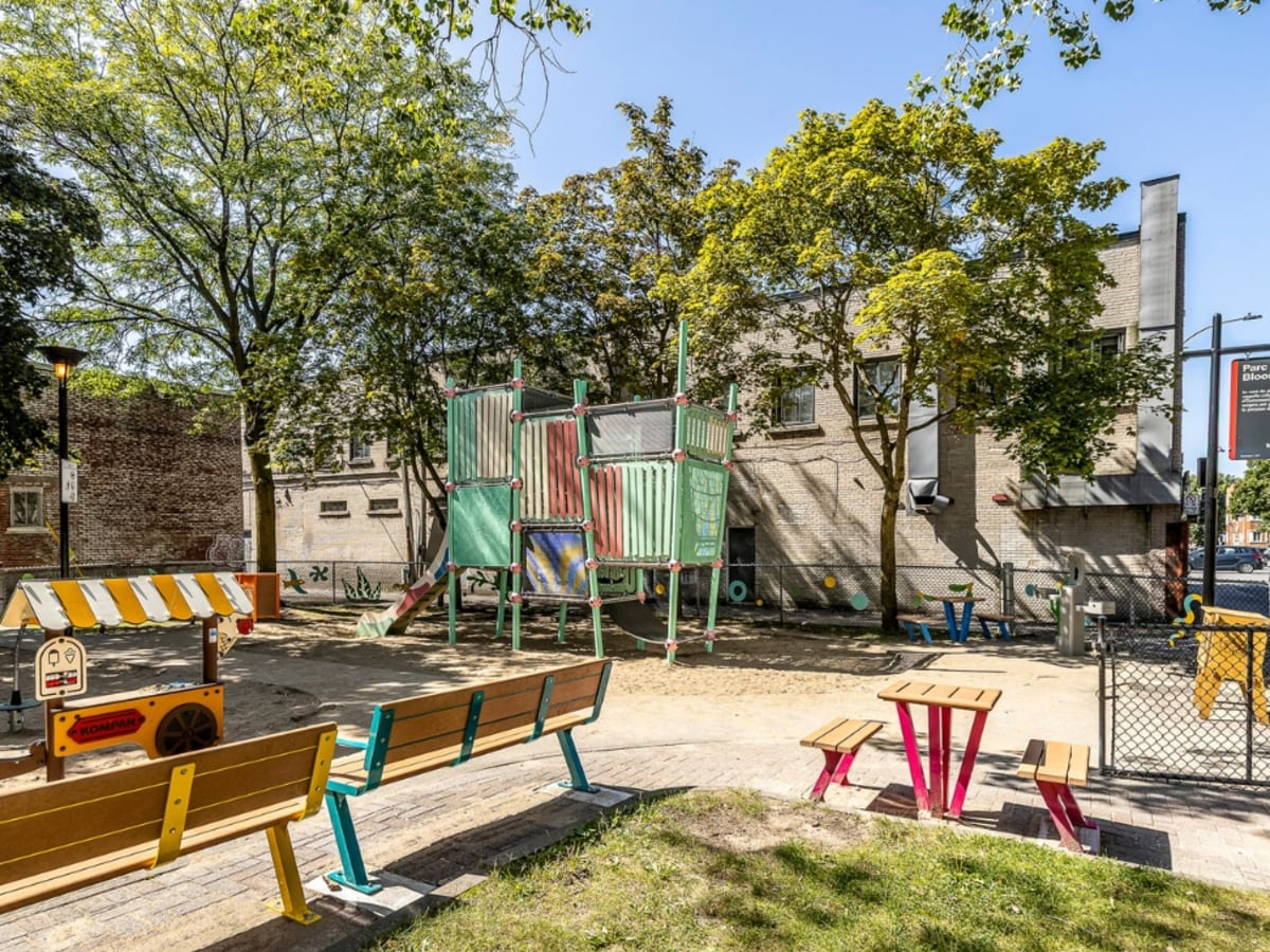 Photo du parc montrant du mobilier coloré tel qu'un banc en bois aux pieds jaunes, un module de jeux avec glissoire aux couleurs pastel, un support à vélo orange et une boîte à livres jaune
