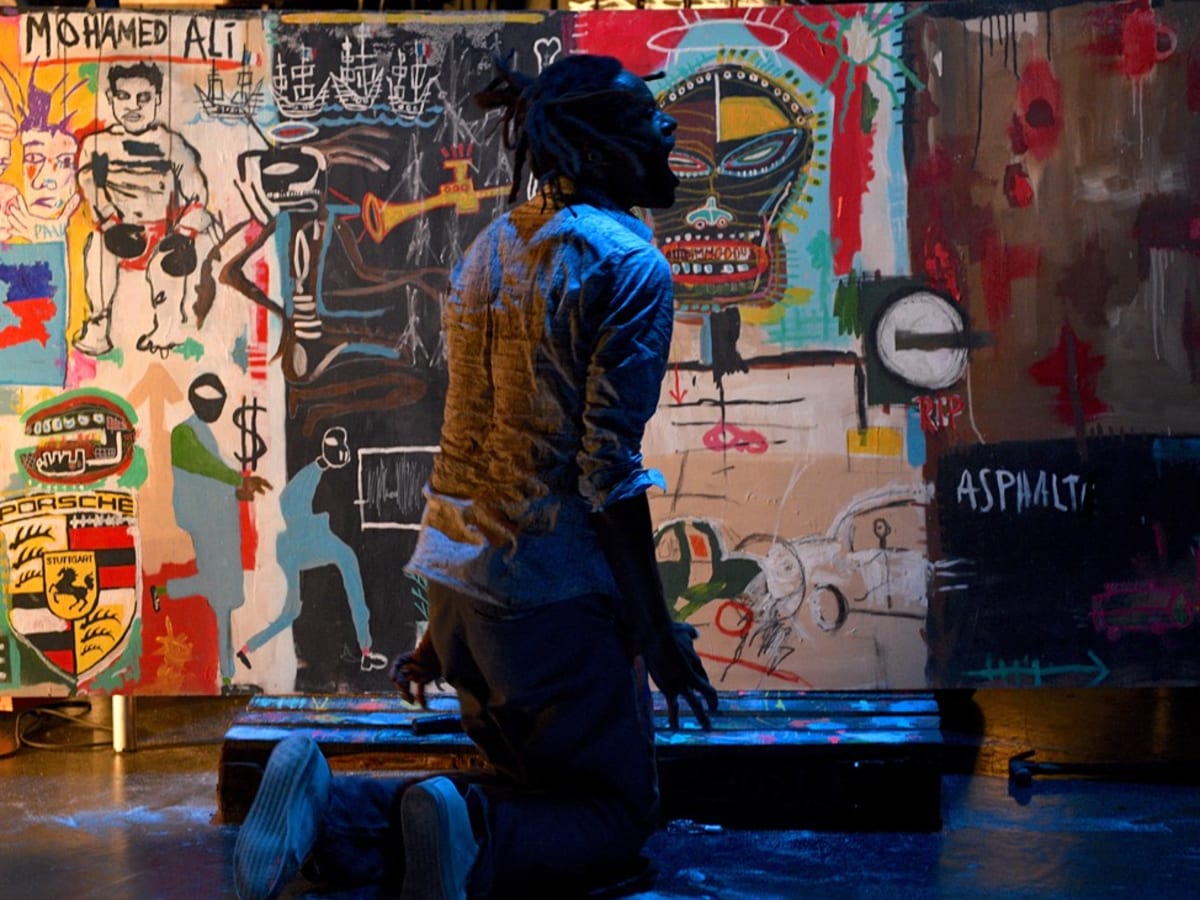 Une personne agenouillée qui crie devant des toiles de Basquiat.