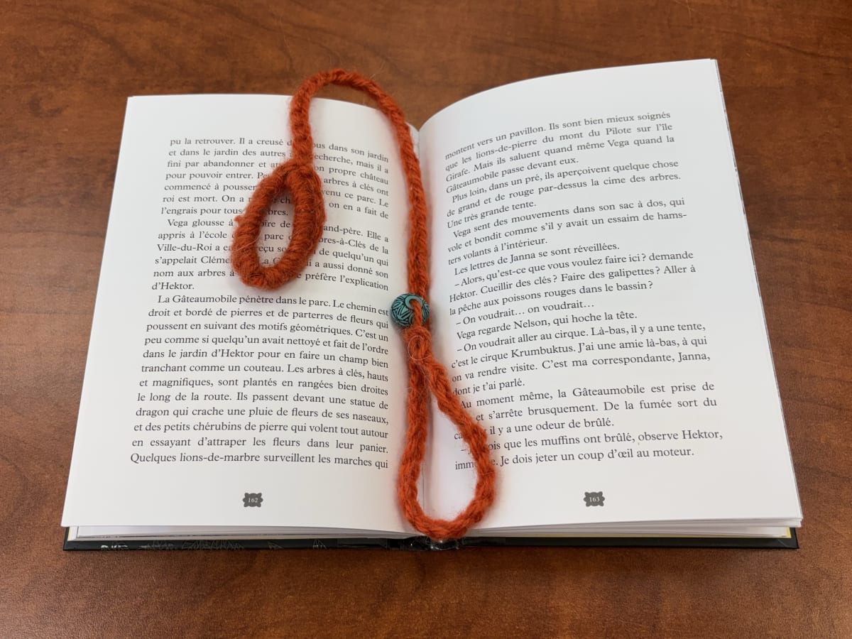 Un livre est ouvert et un bracelet de lecture fait en crochet est au milieu des pages