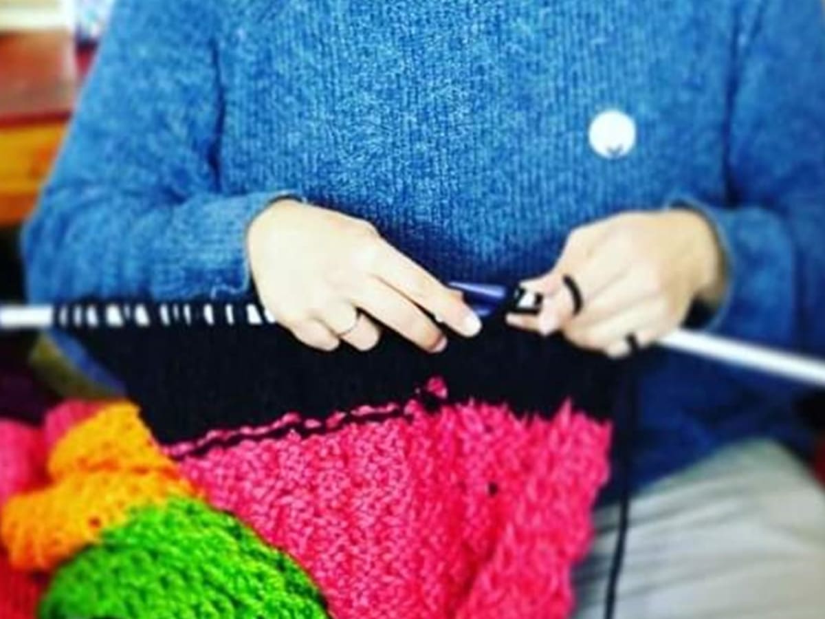 Les mains d'une personne qui tricotte un foulard coloré.