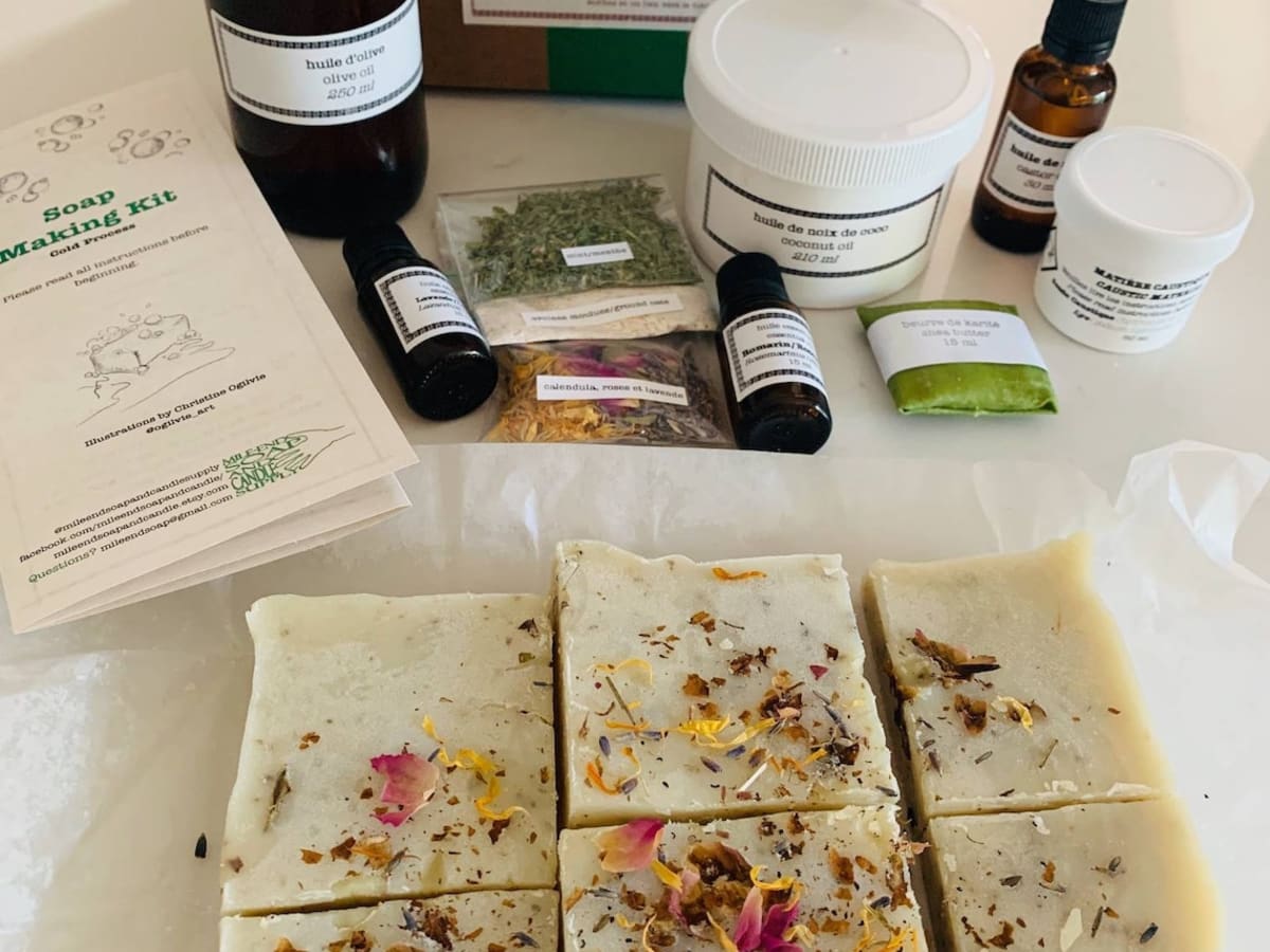 Présentation d'un kit de fabrication de savons naturels, avec les flacons d'huiles essentielles en arrière plan et les savons décorés en premier plan.
