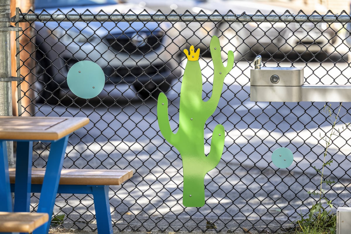 Photos d'éléments en aluminium sur la clôture du parc représentant un cactus vert et jaune et des cercles bleus