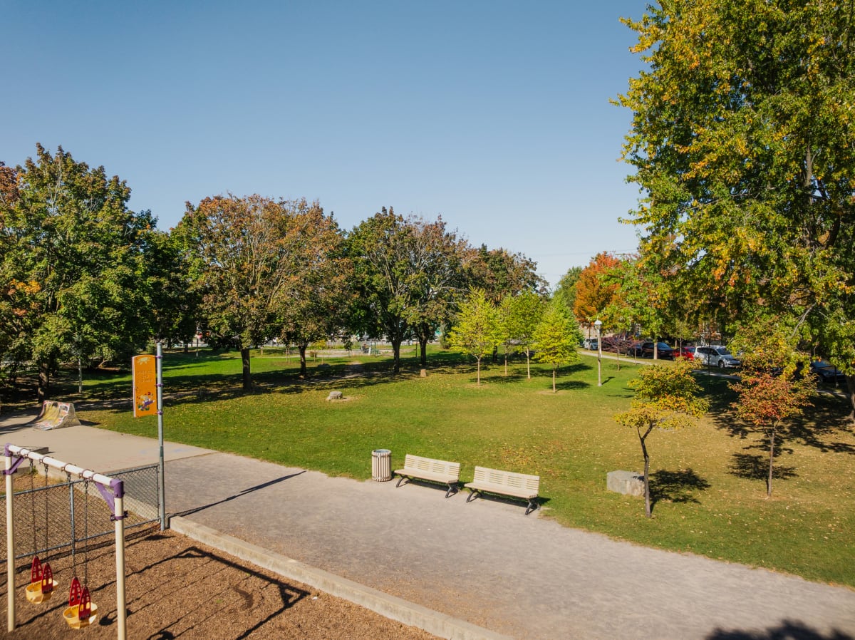 Vue du parc Gabriel-Sagard montrant une étendue d'herbe bordée par un sentier et des bancs en face d'une aire de jeux pour enfants