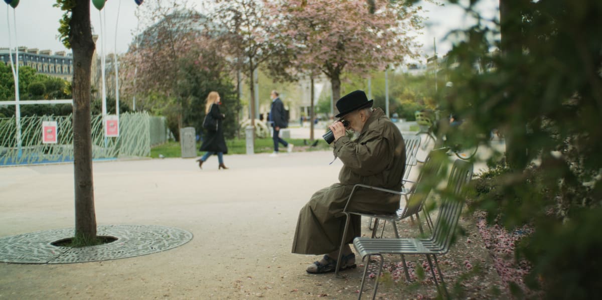 L'acteur Marcel Sabourin assis sur un banc de parc, regarde par terre avec des jumelles.