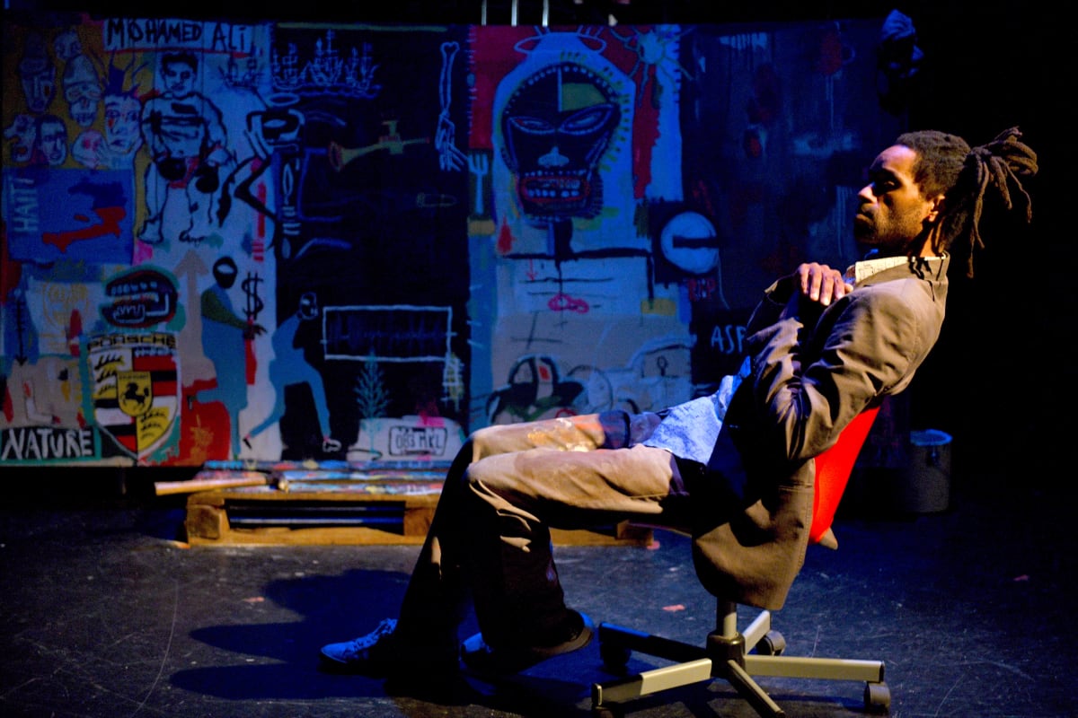 Une personne assise devant des toiles de Basquiat.