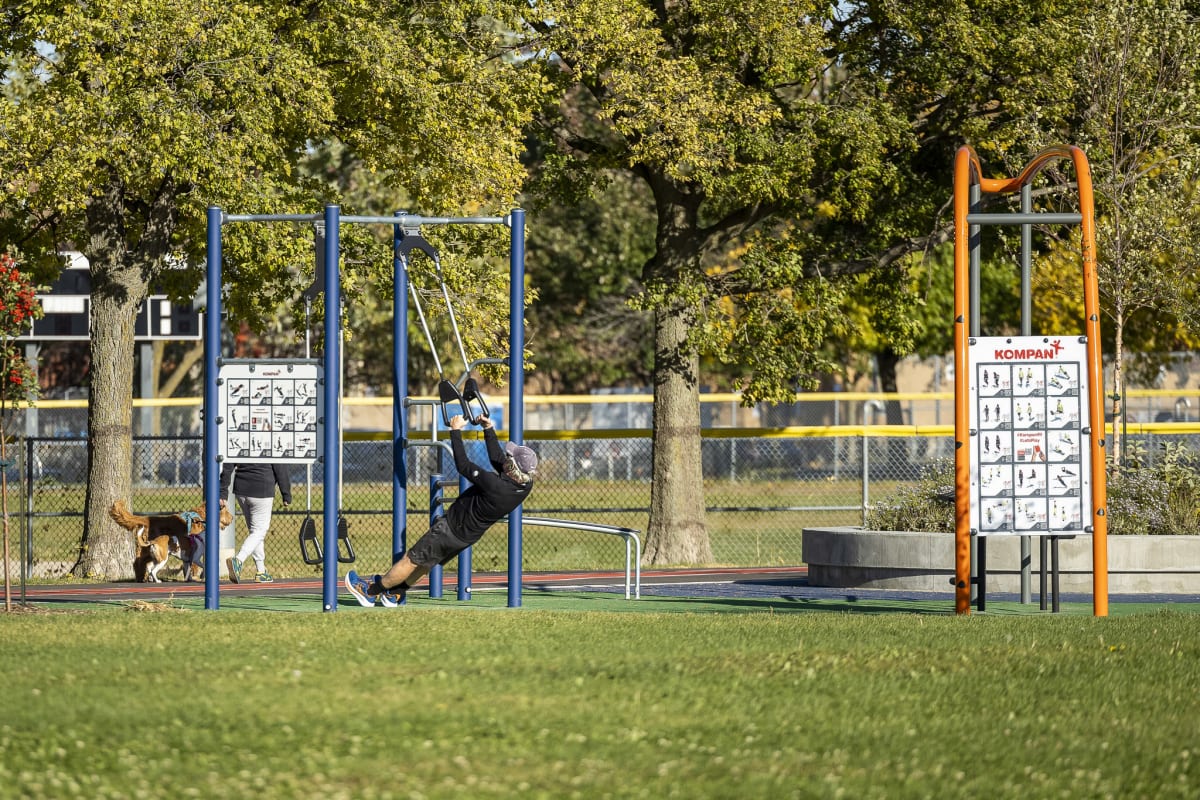 Photo montrant un homme s'entraînant sur les poignées de suspension d'une station d'exercice en plein air, au bord d'une zone gazonnée.