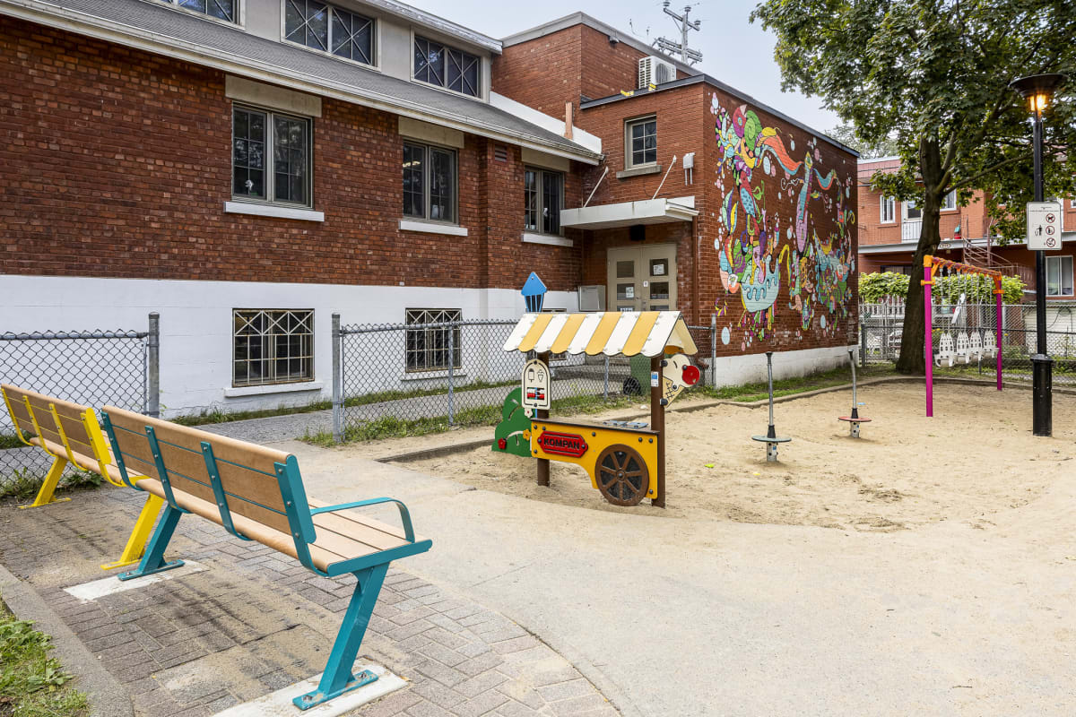 Photo de bancs colorés face à un bac à sable intégrant un module de jeu de la forme d'un kiosque de crème glacée