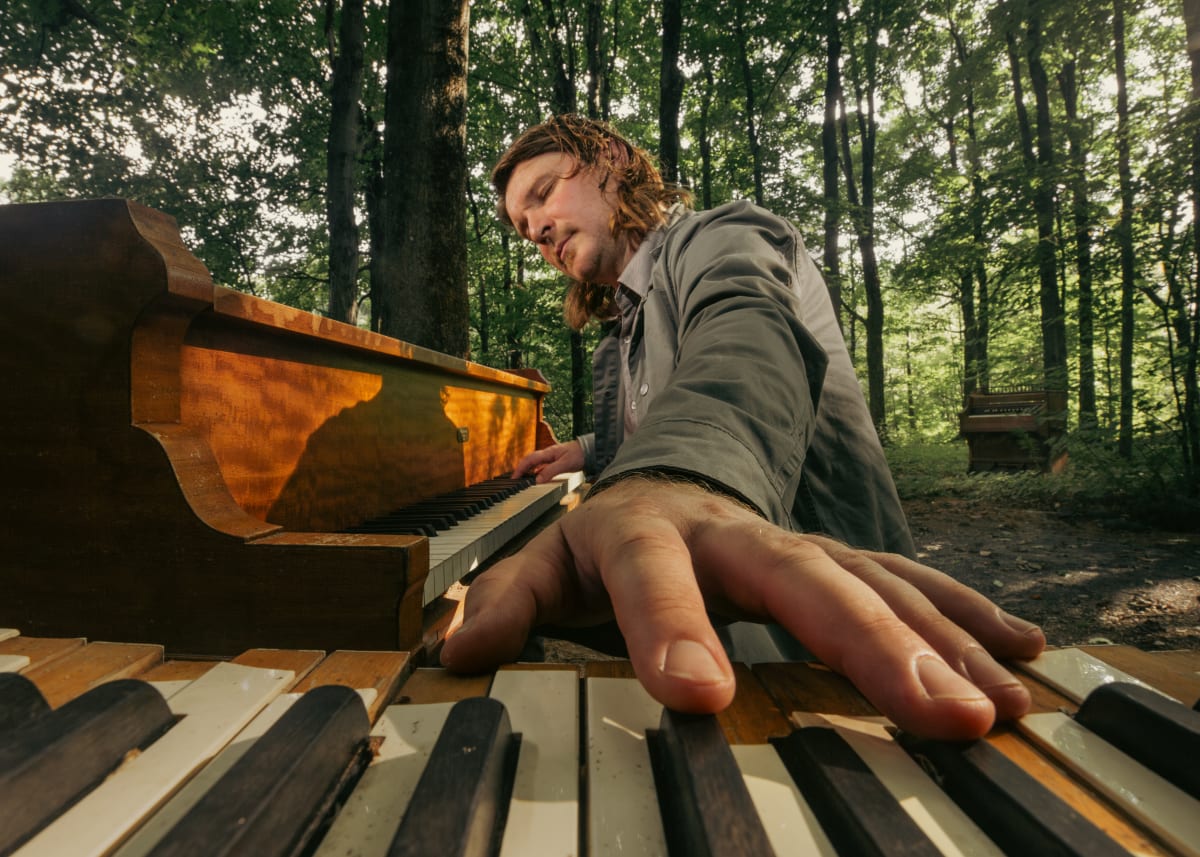 Roman Zavada entrain de jouer du piano au milieu d'une forêt.
