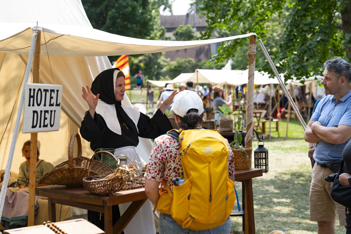 Animatrice habillée en hospitalière donnant des informations historiques à des visiteurs.