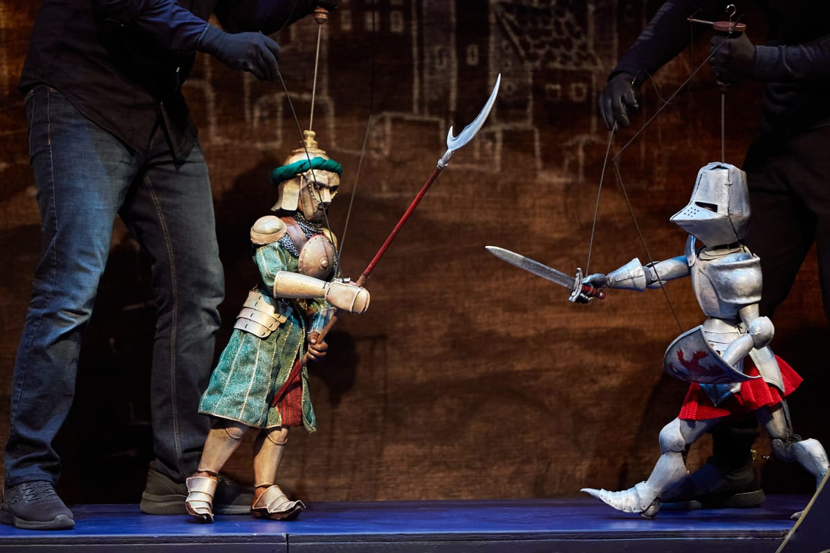Marionnettes manipulées sur scène incarnant des personnages dans une scénographie théâtrale riche en détails et costumes.
