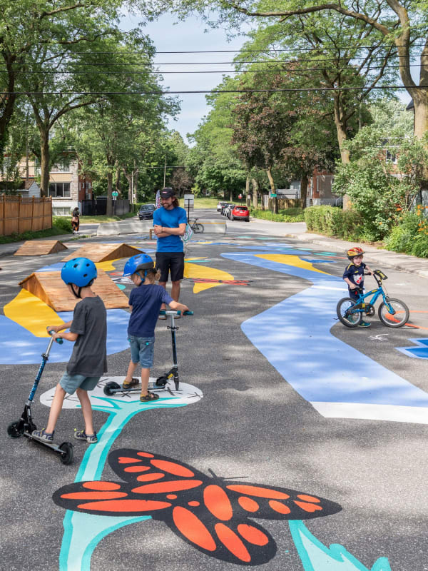 Photo d'enfants à trottinettes et vélo dans le tronçon de la rue De Lotbinière qui a été peint de manière ludique et aménagé pour l'apprentissage du vélo et de la trottinette