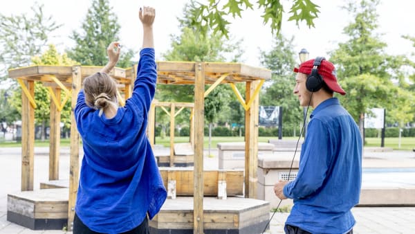 Un jeune homme et une jeune femme en chemise bleu se tiennent devant un gazebo, souriant et discutant.