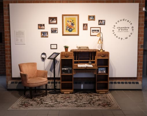 Aperçu de l'exposition Chambre d'écho, avec un fauteuil, un pupitre et des cadres accrochés à un mur blanc.