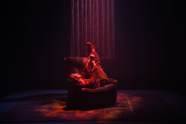 Une personne couchée à l'envers sur un fauteuil, dans une pièce sombre avec un éclairage rouge.