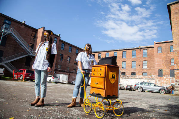 Deux femmes sont debout dans un stationnement avec un chariot servant à distribuer le courrier.