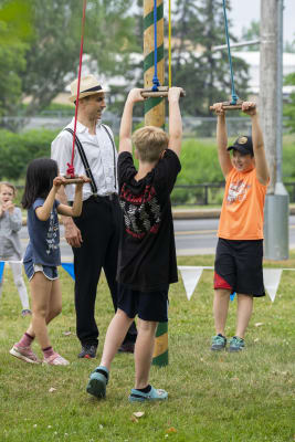 Des enfants s'amusent sur une structure de cirque pendant qu'un homme avec un chapeau les aide.