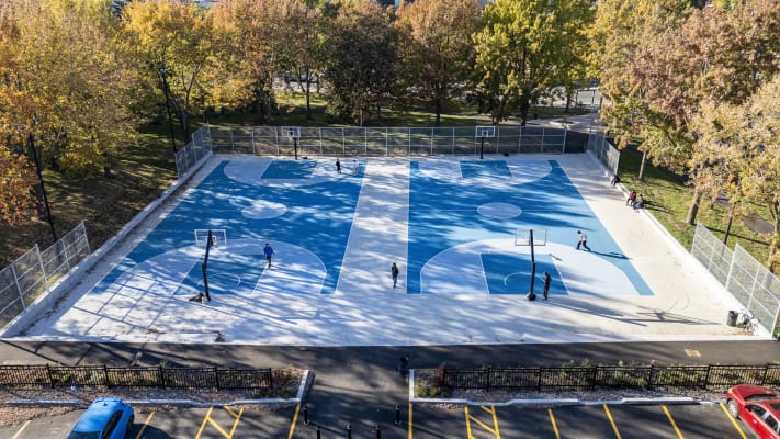 Photo aérienne montrant des personnes jouant au basketball sur les nouveaux terrains fraîchement marqués de peinture bleue et entourés d'arbres