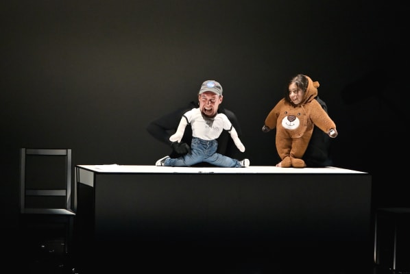 Two people make puppets out of children's clothes, on a small stage.