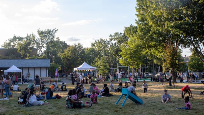 Citoyens et citoyennes assis sur l'herbe, profitant de la fête d'inauguration du parc Montcalm réaménagé dans Rosemont–La Petite-Patrie