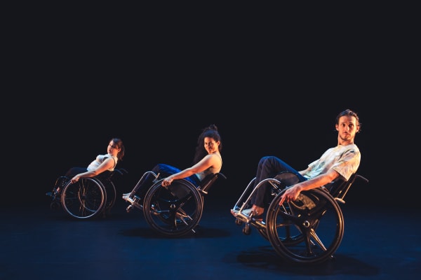 Trois danseurs en chaises roulantes sont alignés sur scène