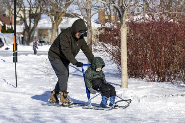 Un père pousse sa fille sur une luge des neiges.