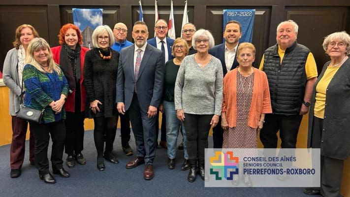 Les neuf membres du Conseil des aînés, le maire Dimitios (Jim) Beis et les conseillers municipaux, tous debous dans la salle du conseil de Pierrefonds-Roxboro.