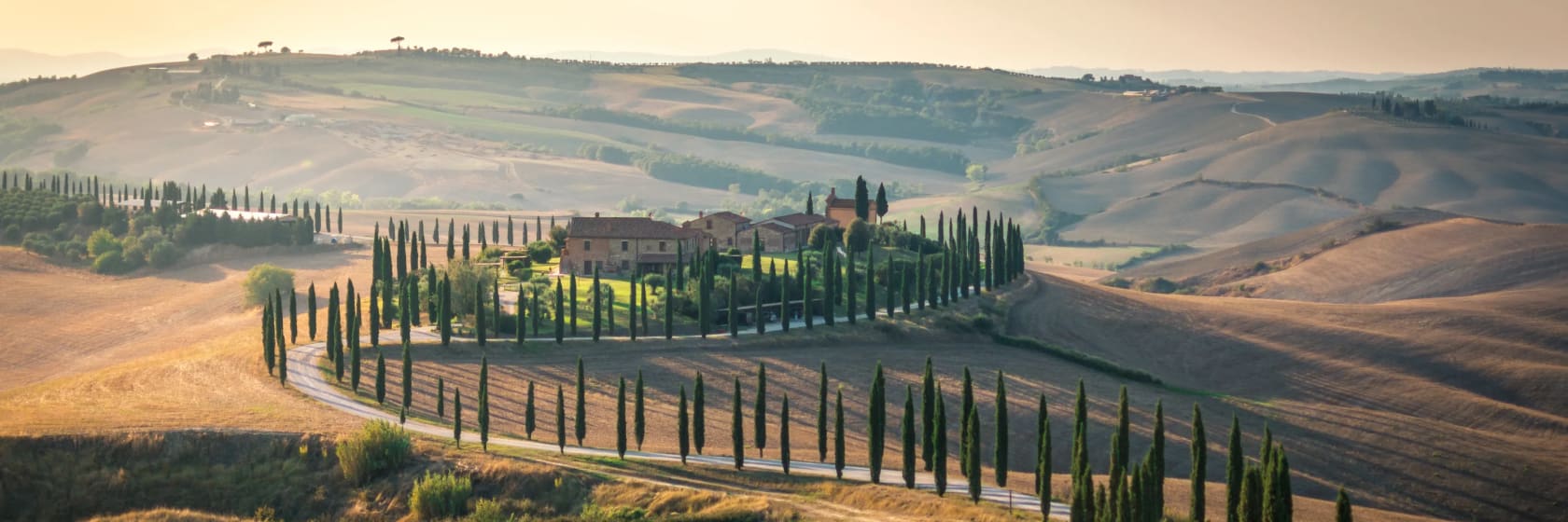 Solnedgang over snoede veje med cypresser i Toscana