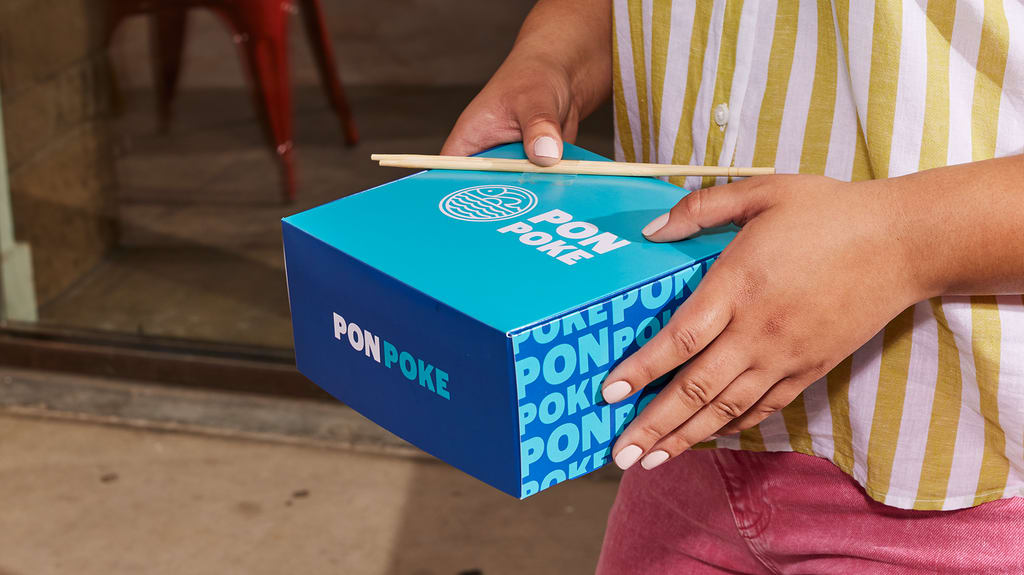 Hands holding a blue food takeaway box with chopsticks