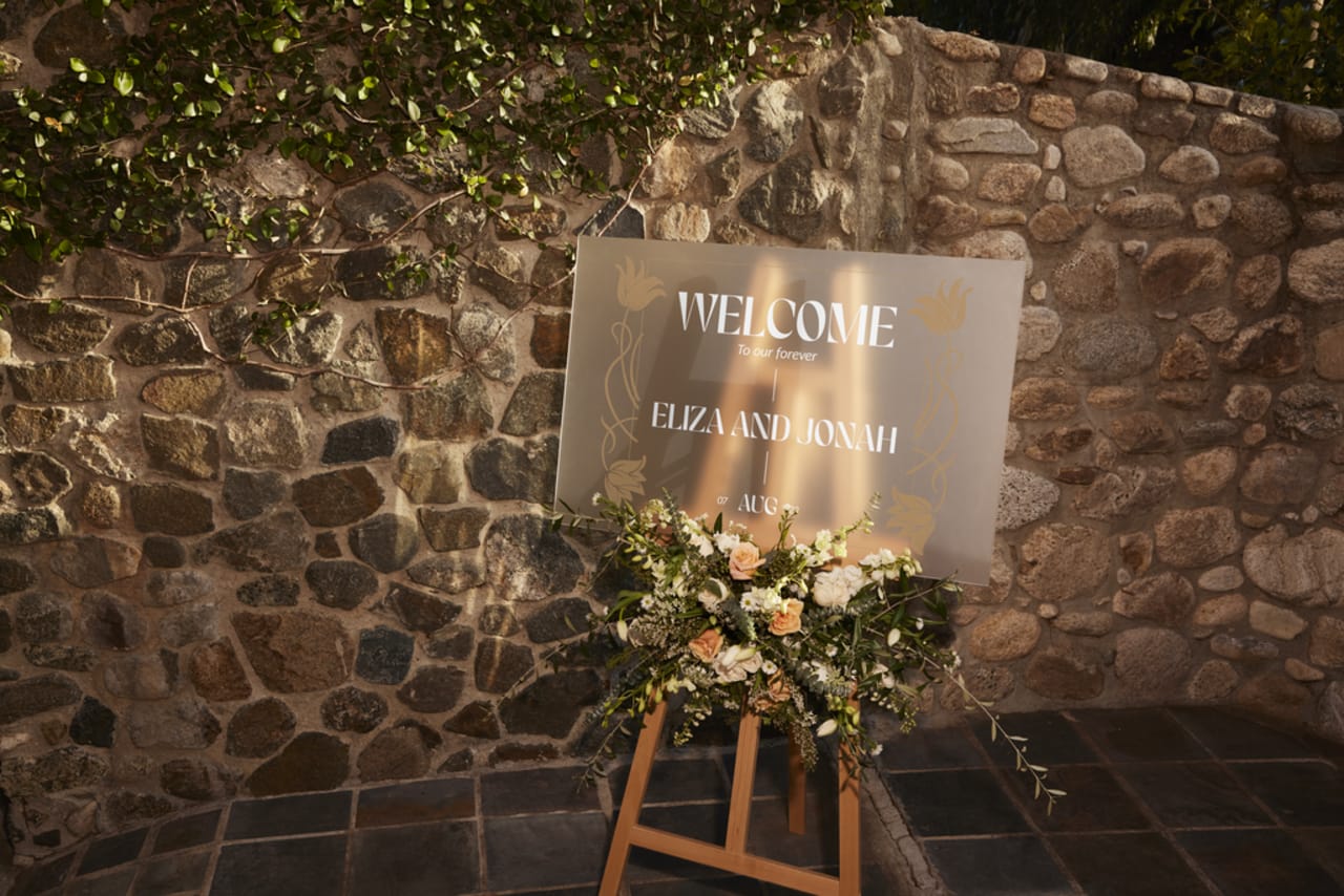 A wedding welcome sign with a bouquet of flowers against a stone wall