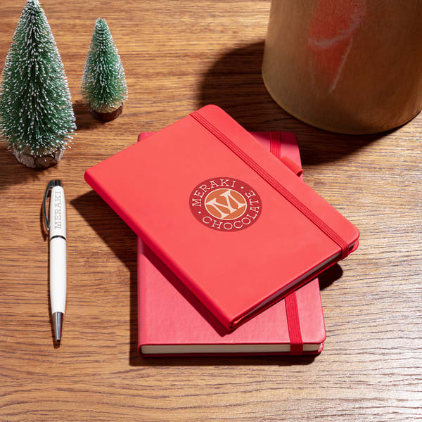 Two custom journals with the brand logo laying on the table next to small decorative Christmas trees