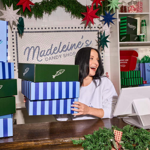 A person holding a stack of branded gift boxes in a retail space decorated for a business holiday event
