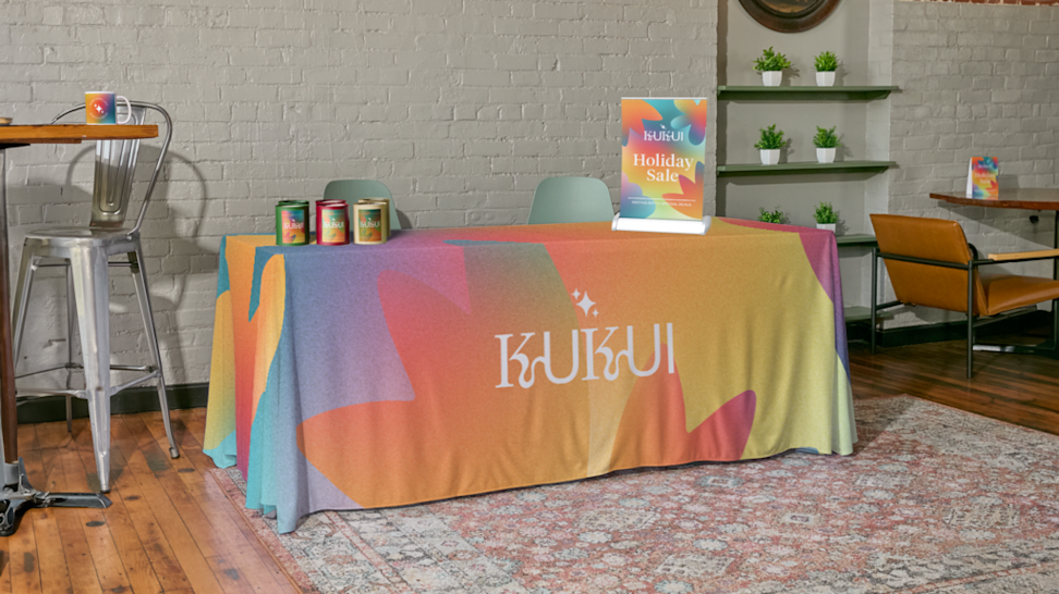 A colorful branded tablecloth on an event booth with a poster and branded products