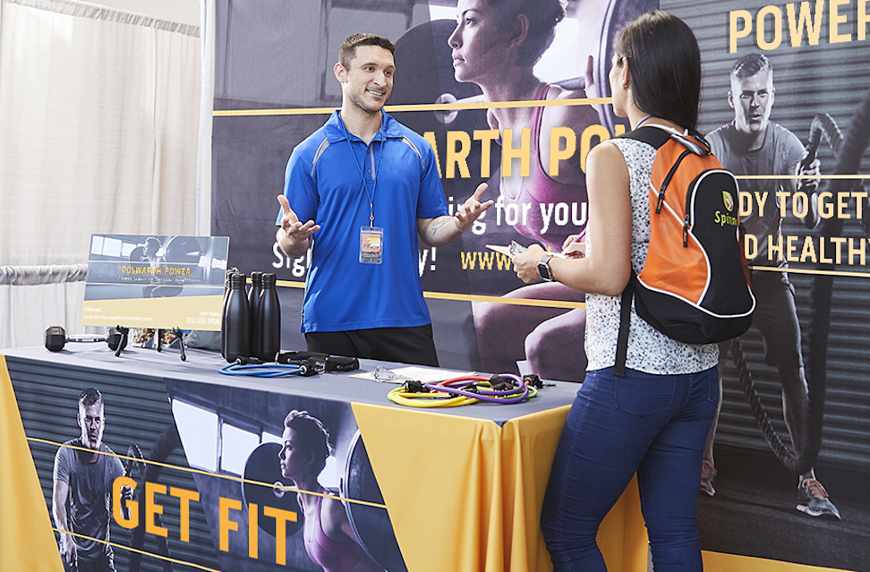 A man and woman talking at an event booth with gym branding